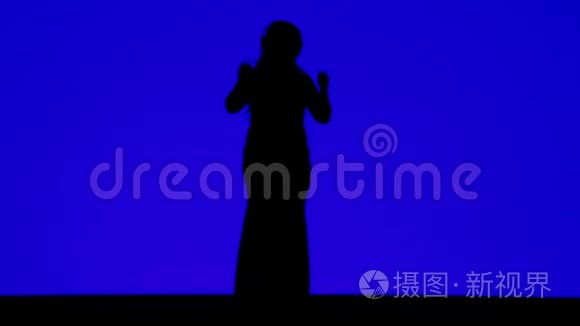 一个戴着耳机的苗条女人在蓝色背景下随着音乐起舞的剪影
