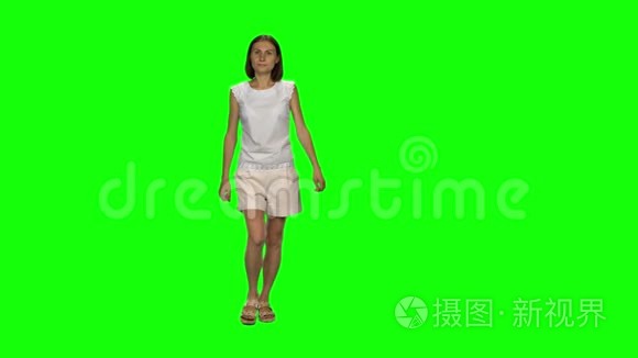 棕色头发和光滑发型的年轻女人平静地走在绿色的屏幕上。 铬钥匙，4k射击。 前景。