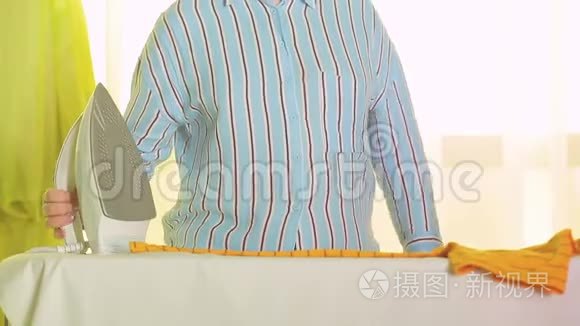 女家庭主妇在家中在熨衣板上熨烫彩色衣服。