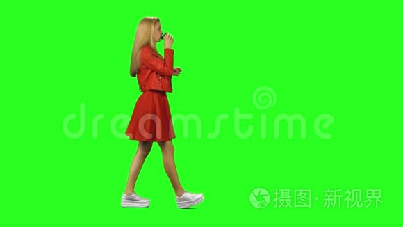 金发女孩平静地走着，在绿色的屏幕背景上喝着咖啡。 铬钥匙，4k射击。 侧写视图。