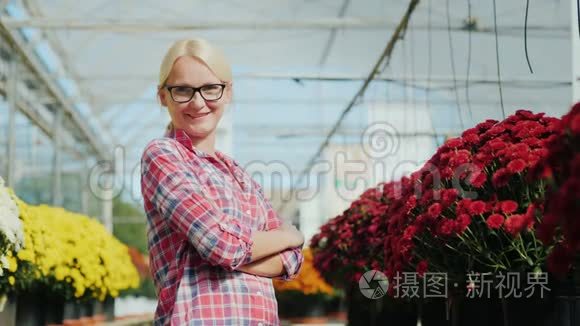 年轻的女人微笑着，看着相机。 它站在植物苗圃里的花的背景上