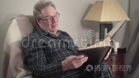 资深白种人退休人员观看相册和微笑的肖像。 老人回忆起晚上在家的回忆
