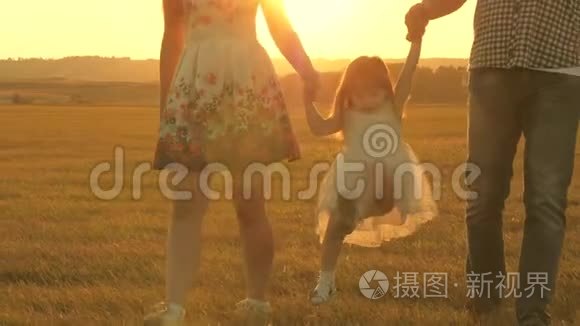 在大自然中和一个小孩子散步。 小女儿在公园的阳光下牵着爸爸和妈妈的手跳着