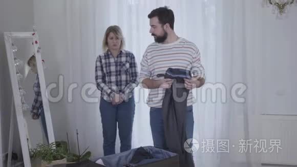 年轻悲伤的白人妇女看着紧张的丈夫收拾手提箱。留胡子的男人离开妻子。分手，离婚