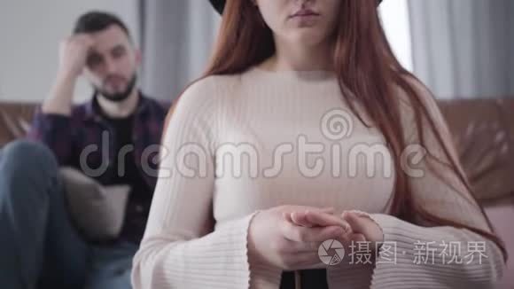 不可辨认的白种人年轻女人摘下结婚戒指，就像坐在后台的胡子模糊的男人。 分手