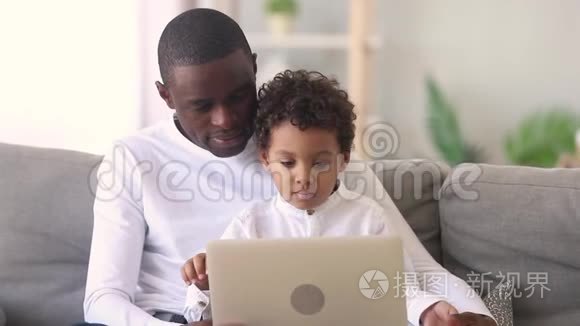 年轻的非洲爸爸教专注的孩子儿子用笔记本电脑
