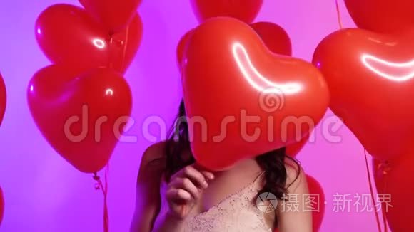 一个年轻快乐的女人把她的脸藏在一个心形的气球后面。