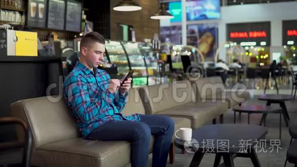 一个年轻人正坐在一家带着电话的咖啡馆里。 这名男子在智能手机上通信，喝咖啡。 特写镜头。