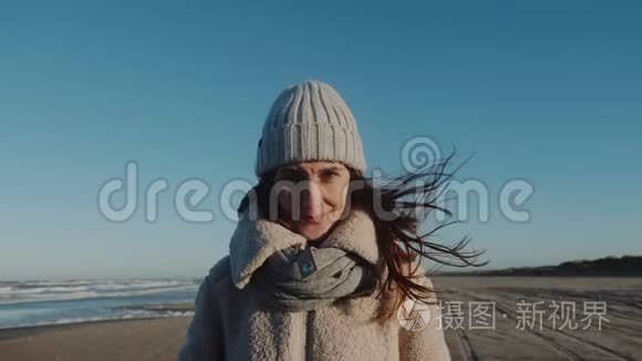 美丽微笑的白人旅游妇女的肖像，看着镜头，在惊人的风冬海岸慢动作。