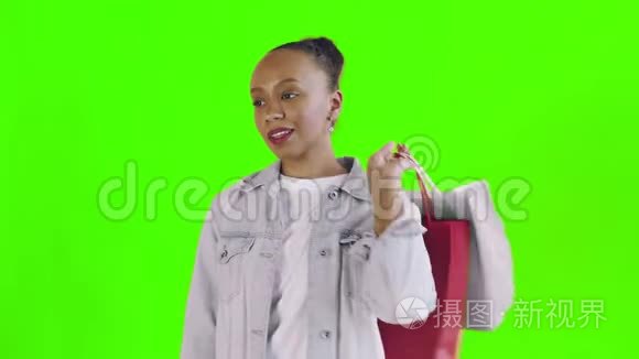美国黑人妇女带着购物袋的肖像是在工作室的绿色背景上通过智能手机谈论的。 让·