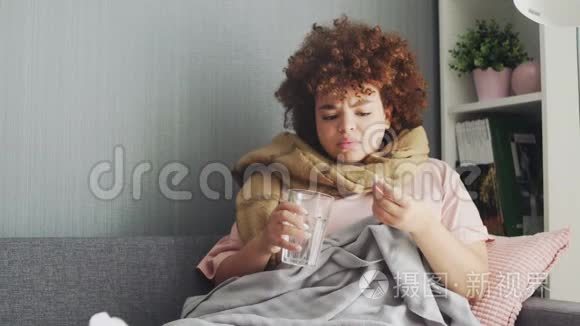 生病的非洲裔美国女孩躺在沙发上，用水吃药。