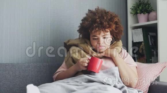一位年轻的非裔美国女孩正在喝热茶，她咳嗽，喉咙痛，用毯子裹着身体