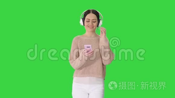 快乐女孩走路听音乐与智能手机戴耳机在绿色屏幕，Chroma键。