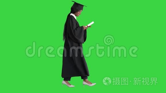 年轻的美国黑人女学生，身穿黑色毕业礼服，持有文凭，在绿色上使用手机