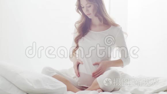 幸福的孕妇抚摸着她美丽的腹部。 怀孕、母性和期望概念