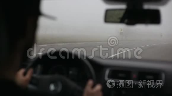 男司机在雾蒙蒙的路上开车.. 从车内铺设现代道路。