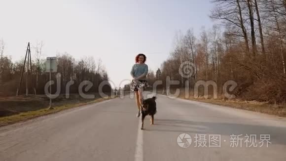 快乐的红头发女人和她的大狗跑向你在日落在道路中间。 慢动作