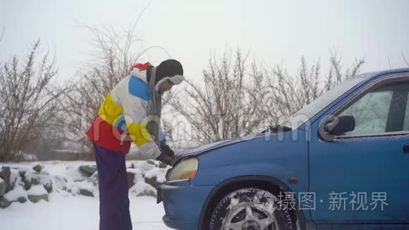 冬天，下着雪。 路上的人汽车出毛病了. 他正试图找出引擎的问题