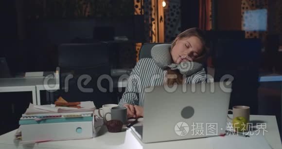 年轻的过度劳累的女人在打开的笔记本电脑前坐在办公桌前睡觉。 女孩办公室经理累了