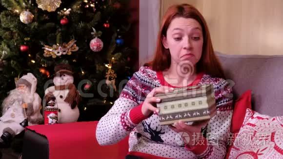 圣诞礼物-悲伤的女人躺在圣诞树附近的沙发上，打开礼物失望和不开心。 概念