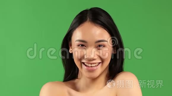 美丽的年轻亚洲女人微笑着，看着绿背景上的摄像机