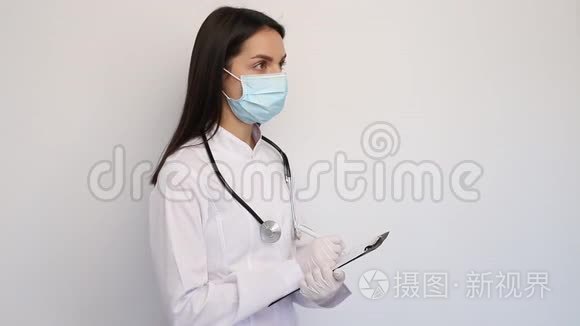 友好的女医生穿着白色的医用外套手套和防护面罩，把诊断写在客户卡上，