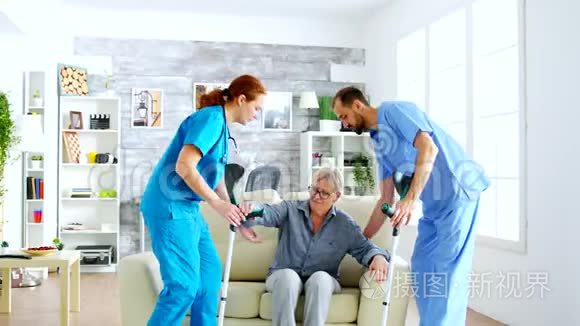 女医生和她的助手用拐杖帮助老妇人从沙发上站起来