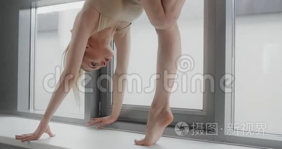 迷人的金发女郎在瑜伽工作室的窗台上慢动作地表演杂技体操技巧，灵活多变