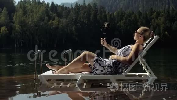 女性拍摄手持电影万向节稳定智能手机。 女孩躺在码头晒太阳自拍。 博客