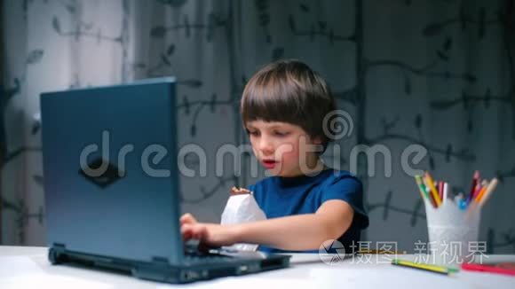 一个男孩坐在学校的办公桌前，用笔记本电脑键盘打字。