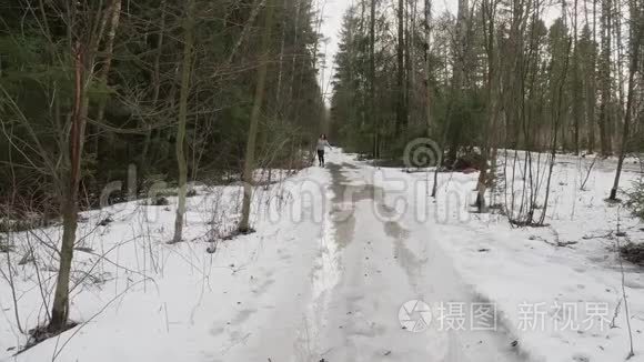 穿着运动服的女人朝镜头跑去。 她在森林里雪上奔跑。 冬天慢跑。