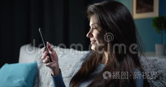 快乐的女人在沙发上使用智能手机