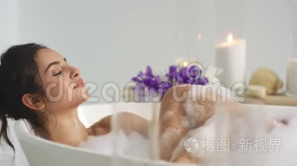 特写放松的女人用泡沫在家里洗澡。 女人吹着泡沫