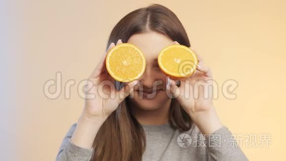 可爱的女孩脸上带着一半的橘子水果做鬼脸，十几岁的孩子在演播室背景上玩得开心，心情积极，自负