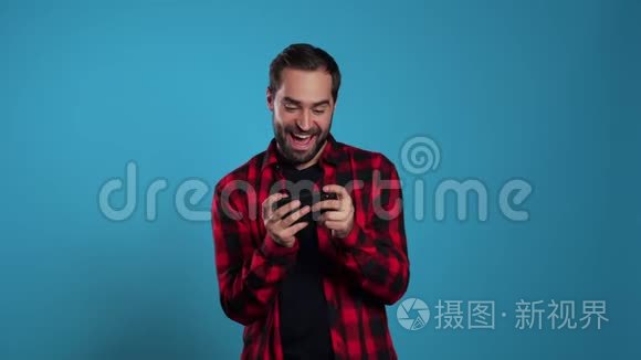 帅哥在蓝色工作室墙上的智能手机上玩游戏。 使用现代技术-应用程序，社交网络。