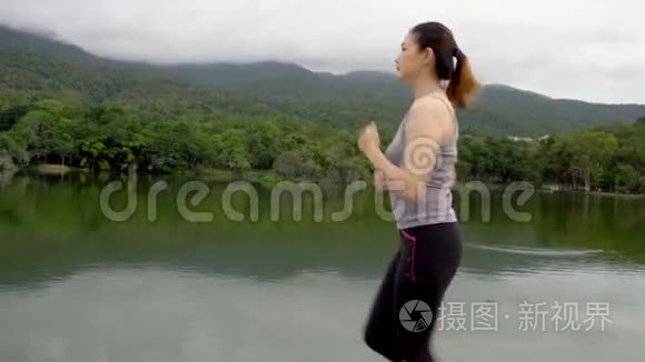 年轻健康的亚洲女人在一个带湖的户外自然公园晨跑时停下来喝水，擦汗