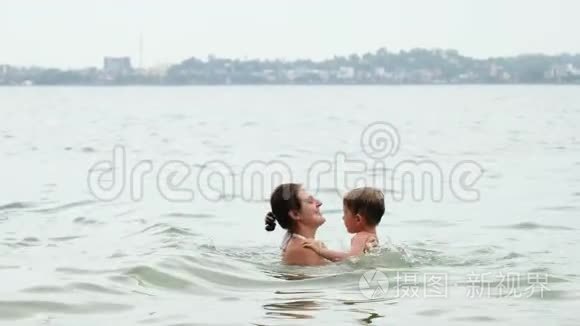 4K镜头，快乐的微笑母亲拥抱和呕吐，她的小儿子在海洋游泳