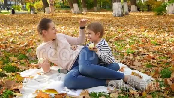 带着年轻妈妈躺在秋天公园的毯子上吃苹果的笑笑小男孩4k视频