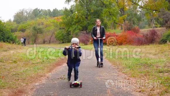 4k视频：4岁的微笑男孩骑着滑板车和他的母亲在秋天公园