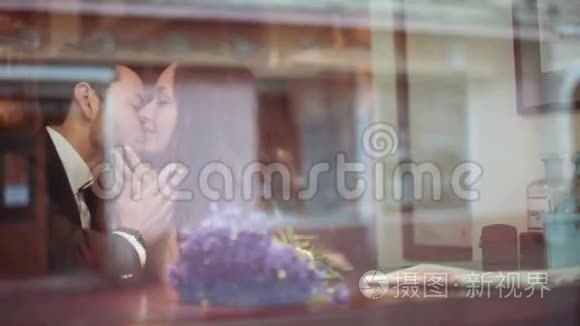 年轻的男人和漂亮的黑发欧洲女人穿着白色连衣裙，在窗边的咖啡馆里热情地接吻