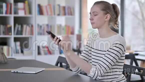 快乐的年轻女子在图书馆用智能手机交谈