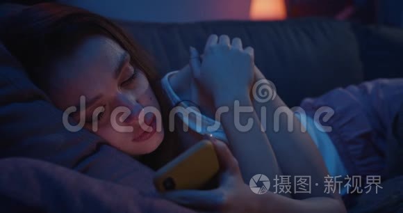 一个孤独的年轻女子躺在沙发上，晚上使用智能手机。 一位沮丧的千禧女性