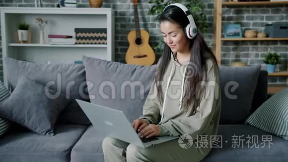 戴着耳机在家里沙发上听音乐和使用笔记本电脑的美女