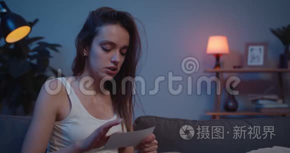 一个不快乐的年轻女子坐在沙发上愤怒地撕扯照片并扔掉。伤心的女孩哭泣