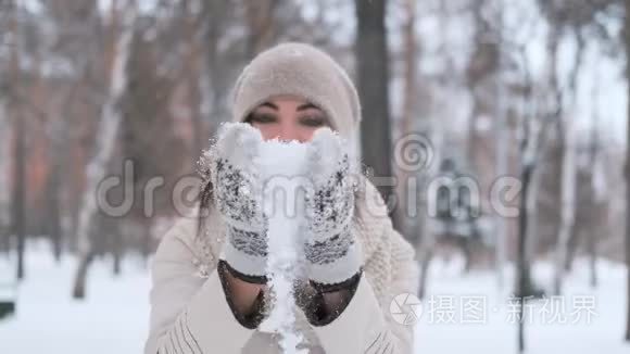 美丽的年轻女子，一头乌黑的头发，在冬天的公园里，拍着手套，雪微笑着，非常高兴。 慢动作