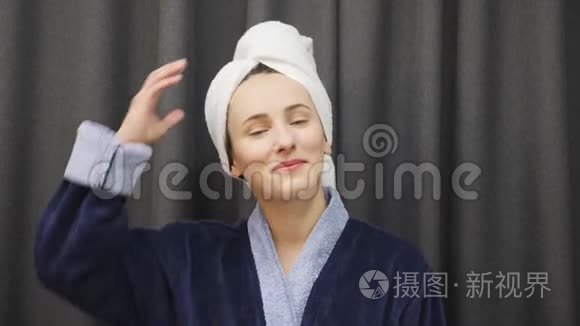 女人从头上摘下毛巾，摸湿头发。 年轻的女性穿着蓝色浴袍，洗澡后头发湿透。 健康与美容