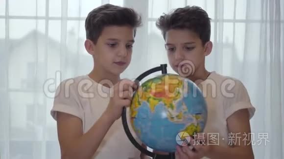 黑种人白人小学生拿着地球仪，向他的孪生兄弟解释地理的特写照片。 兄弟姐妹
