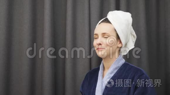 年轻女性从头上摘下毛巾，洗澡后抚摸她湿漉漉的头发。 洗澡后穿蓝色浴袍的女士