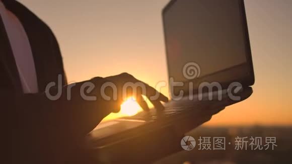 特写：程序员在日落时分用手在笔记本电脑键盘上打字，俯瞰屋顶.. 一个商人在远程工作