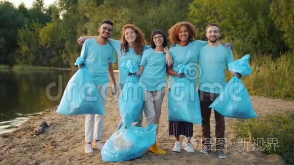 多种族的志愿者在清洁的湖面上拥抱微笑的垃圾袋